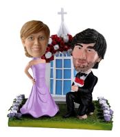 Custom bobblehead of a couple that the groom is proposing to his wife-to-be with a bunch of rose. The custom bobbleehad groom is in full black smart suit getting one knee on the ground holding a bunch of bloomy roses. It seems like he is say â€œwill y